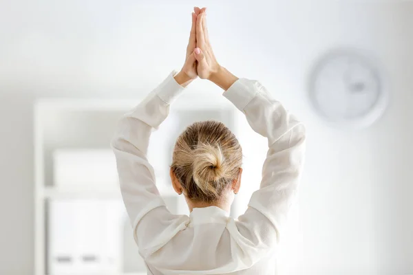 Young businesswoman practicing yoga in office, back view