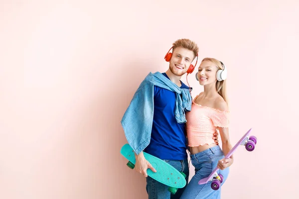 Jeune couple avec planches à roulettes écoutant de la musique sur fond de couleur — Photo