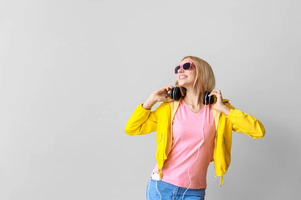 Mooie jonge vrouw luisteren naar muziek op lichte achtergrond — Stockfoto