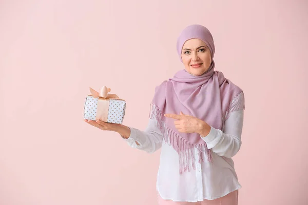 Schöne reife muslimische Frau mit Geschenkbox auf farbigem Hintergrund — Stockfoto