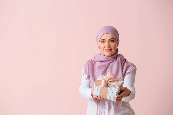 Beautiful mature Muslim woman with gift box on color background — Stock Photo, Image