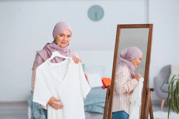 Mulher muçulmana madura bonita com nova camiseta perto do espelho em casa — Fotografia de Stock