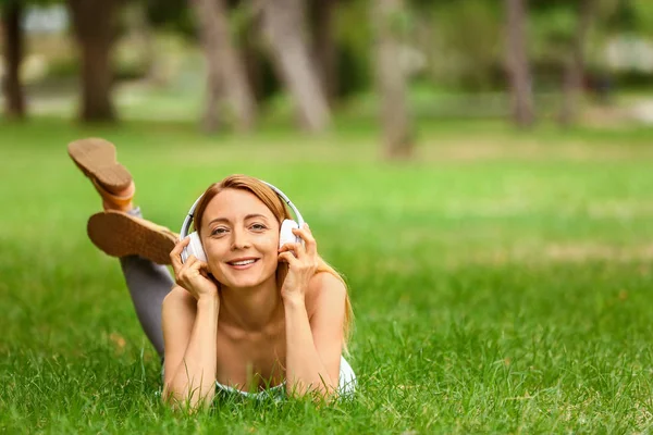 Woman listening to music while relaxing in park — Stock Photo, Image