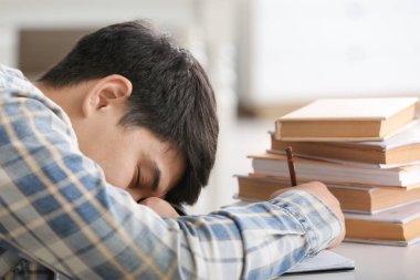 Yorgun Asyalı öğrenci masada uyuyor