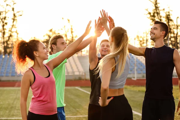 Groep sportieve jongeren die de handen in elkaar zetten in het stadion — Stockfoto