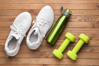 Ahşap arka planda spor su şişesi, ayakkabı ve halter