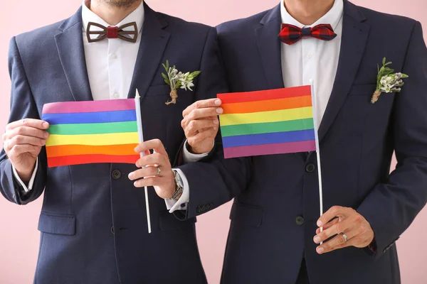 Feliz pareja gay con banderas LGBT en el día de su boda contra el color de fondo — Foto de Stock