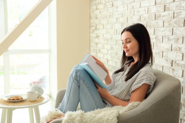 Evde kitap okuyan güzel genç bir kadın.