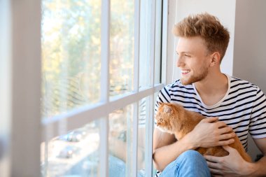 Evde pencere yakınında sevimli kedi ile genç adam
