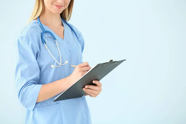 Female nurse with stethoscope and clipboard on color background — Stock Photo, Image