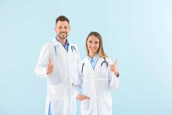 Male and female doctors showing thumb-up on light color background — Stock Photo, Image