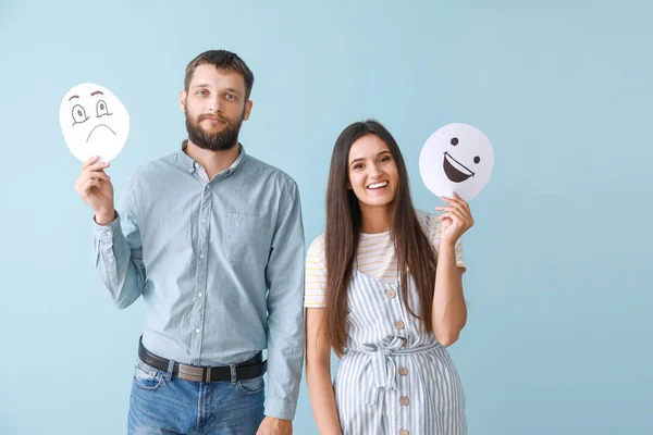 Pareja feliz sosteniendo hojas de papel con emoticonos dibujados sobre fondo de color — Foto de Stock