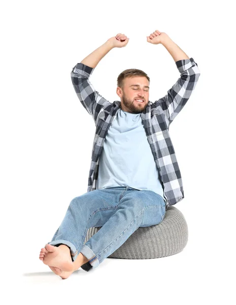 Snygg ung man avkopplande på sittpuff mot vit bakgrund — Stockfoto