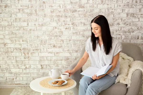 Belle jeune femme buvant du thé tout en lisant le livre à la maison — Photo