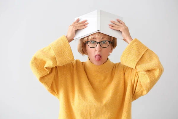 Portrait of funny middle-aged woman with book on light background — Stock Photo, Image