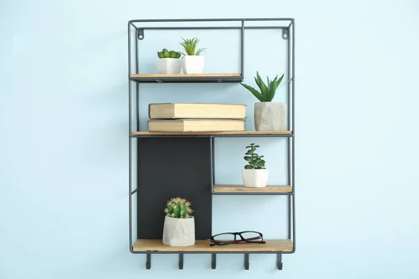 Shelves with books and houseplants on color wall