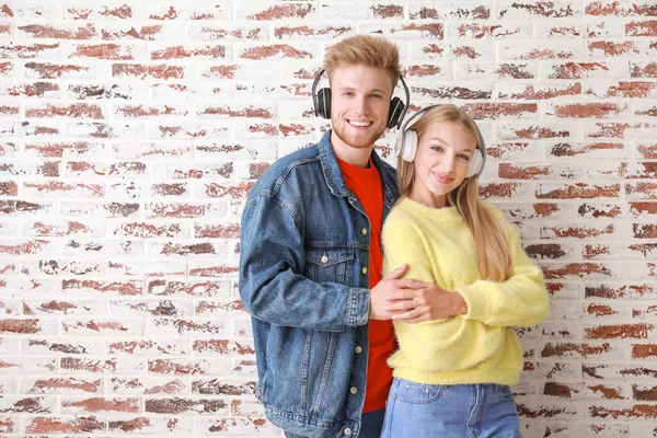 Pareja joven escuchando música contra la pared de ladrillo — Foto de Stock