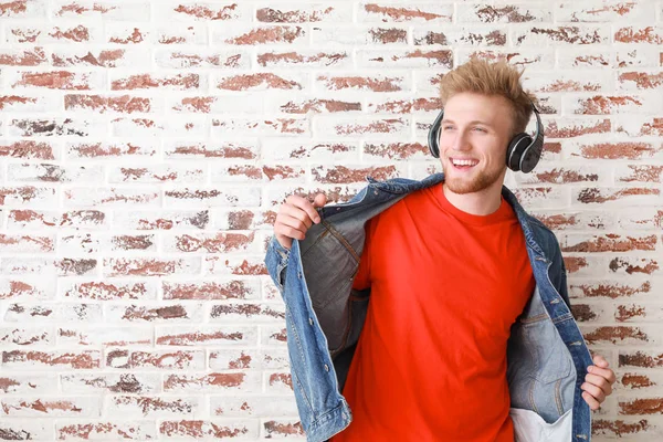 Knappe jonge man luisteren naar muziek tegen bakstenen muur — Stockfoto