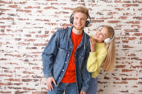 Jovem casal ouvindo música contra parede de tijolo — Fotografia de Stock