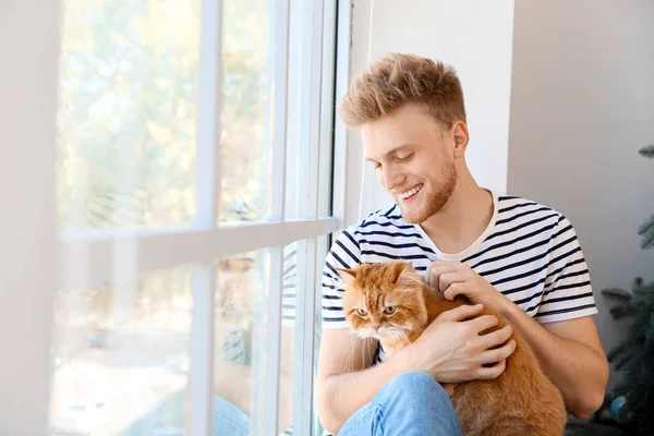 Young man with cute cat near window at home