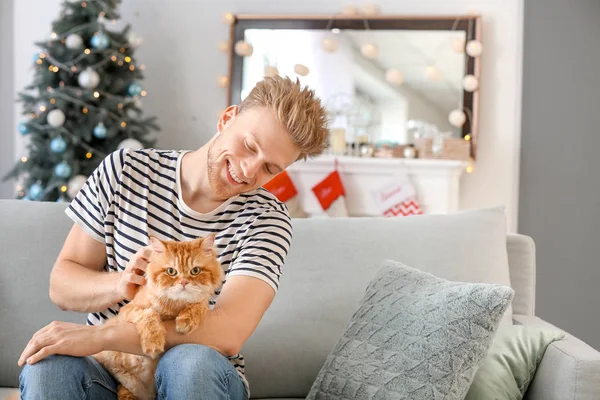 Young man with cute cat at home on Christmas eve