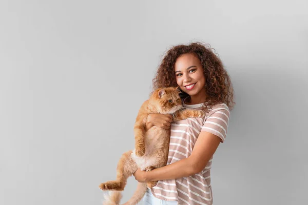 Young African-American woman with cute cat on light background — Stock Photo, Image