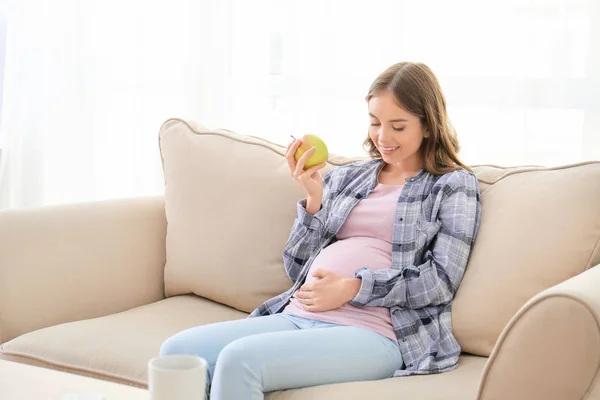 Krásná těhotná žena s jablkem seděla doma na pohovce — Stock fotografie