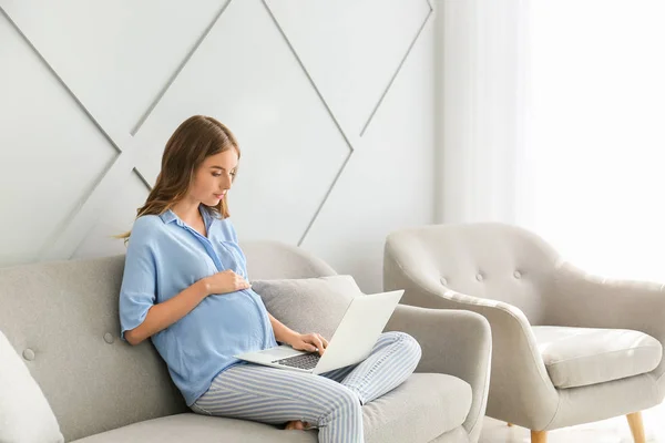 Hermosa mujer embarazada con portátil sentado en el sofá en casa — Foto de Stock