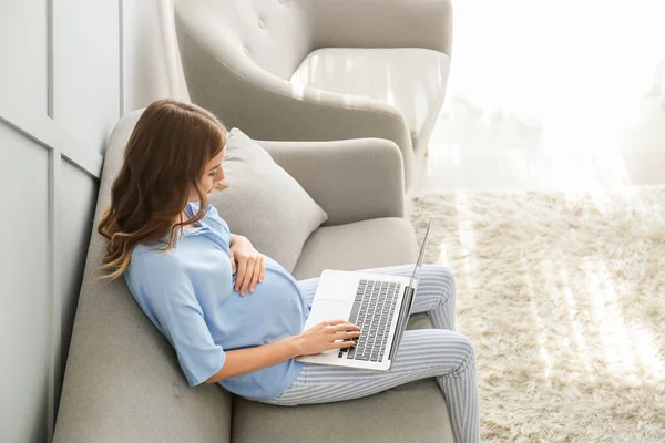 Hermosa mujer embarazada con portátil sentado en el sofá en casa — Foto de Stock