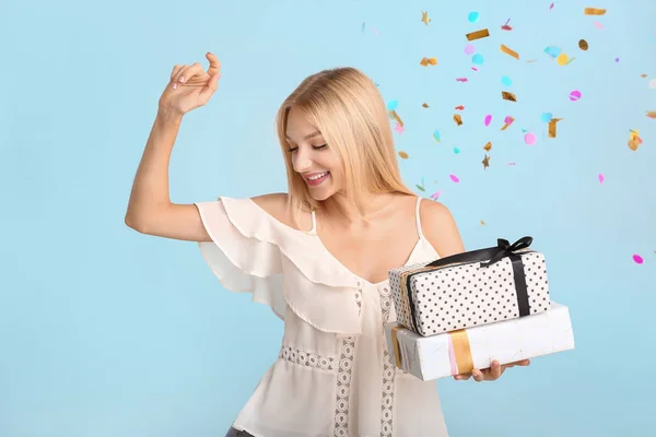 Belle jeune femme avec des cadeaux et des confettis tombant sur fond de couleur — Photo