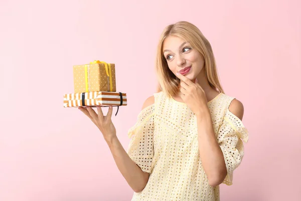 Doordachte jonge vrouw met cadeaus op kleur achtergrond — Stockfoto
