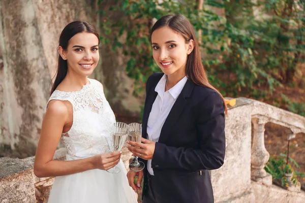 Beautiful lesbian couple with glasses of champagne on their wedding day outdoors — Stock Photo, Image