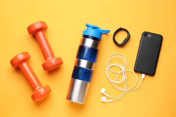 Sports water bottle, dumbbells, mobile phone and fitness tracker on color background — Stock Photo, Image