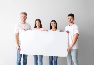 Açık arka planda boş poster tutan şık giysiler içinde genç bir grup