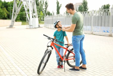 Baba dışarıda bisikletsürmeden önce kask koymak için oğlu yardım
