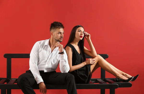 Elegante jovem casal sentado no banco contra fundo de cor — Fotografia de Stock