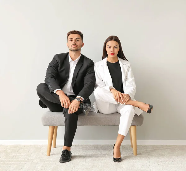 Elegante jovem casal sentado no banco perto da parede branca — Fotografia de Stock