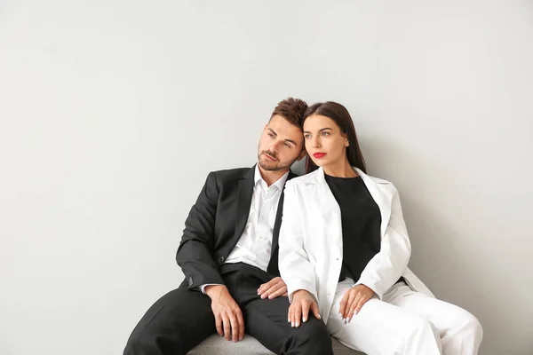 Elegante jovem casal sentado no banco perto da parede branca — Fotografia de Stock