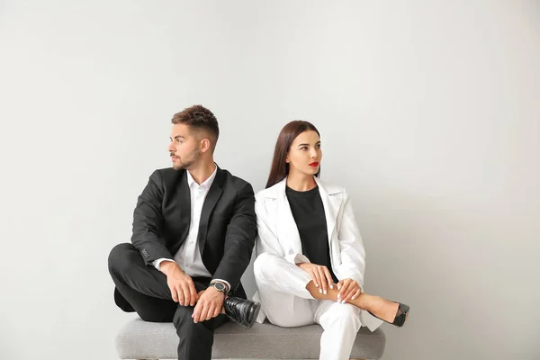 Elegante jovem casal sentado no banco perto da parede branca — Fotografia de Stock