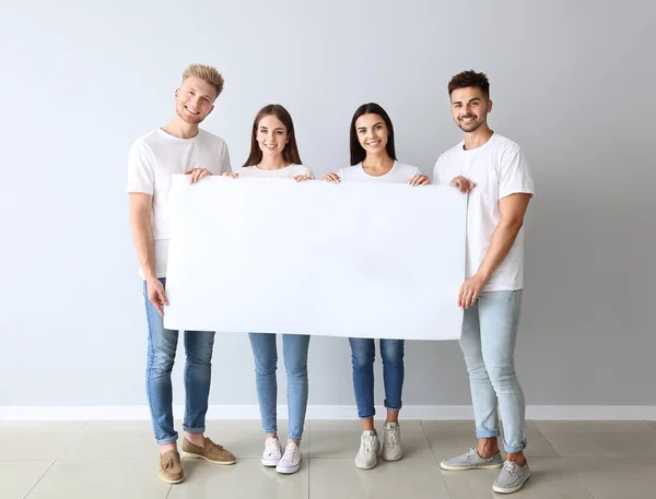 Grupo de jóvenes en ropa casual con estilo y con cartel en blanco cerca de la pared de luz — Foto de Stock