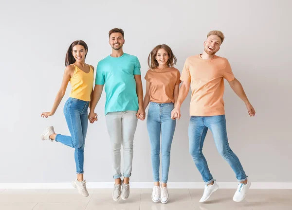Группа прыгающих молодых людей в стильной повседневной одежде возле светлой стены — стоковое фото
