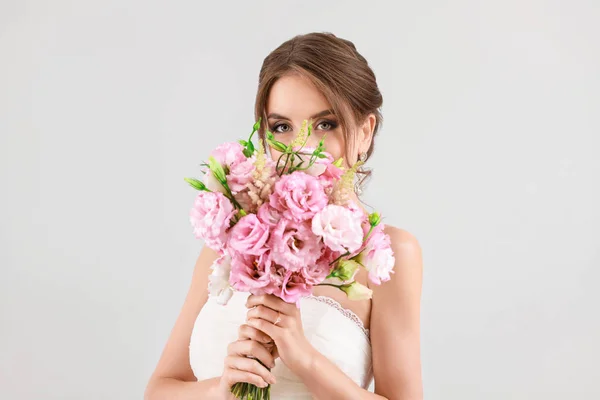 Portrait of beautiful young bride with wedding bouquet on light background — Stock Photo, Image