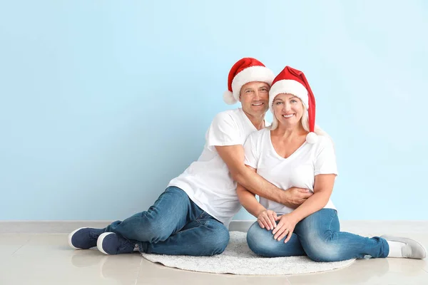 Happy äldre par i Santa Claus hattar sitter nära ljus vägg — Stockfoto