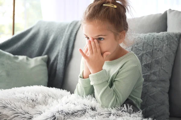 Sick little girl sitting on sofa at home — Stock Photo, Image