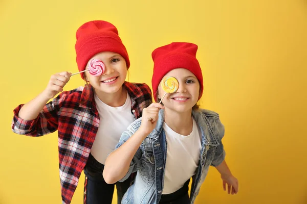 Portrait of happy twin girls with lollipops on color background — Stock Photo, Image