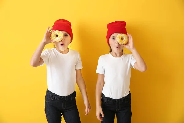 Portrait of surprised twin girls with tasty donuts on color background — Stock Photo, Image