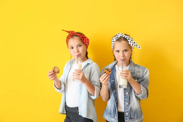 Portrait of cute twin girls with cookies and glasses of milk on color background — Stock Photo, Image