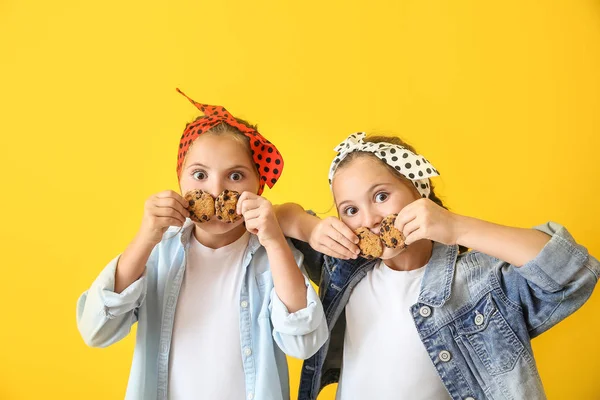 Ritratto di divertenti ragazze gemelle con biscotti sullo sfondo a colori — Foto Stock