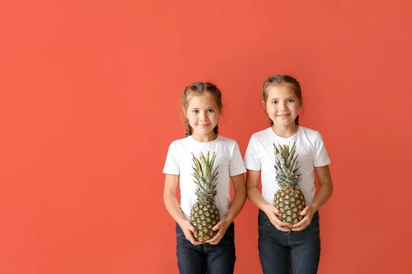 Portrait of cute twin girls with pineapples on color background — Stock Photo, Image