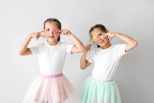 Ritratto di divertenti ragazze gemelle con lecca-lecca su sfondo chiaro — Foto Stock